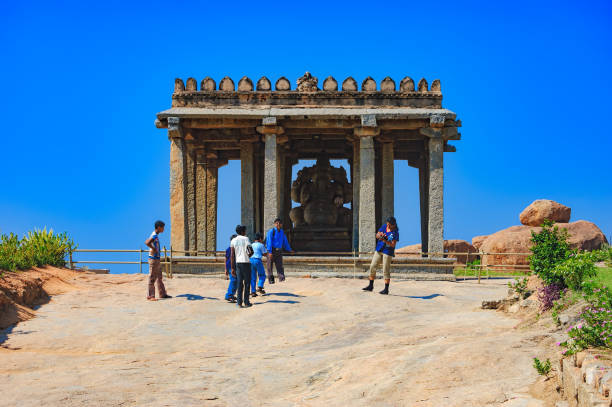 Hampi, India - November 19, 2012: Unidentified Indian tourists visit to the famous landmark. Hindu people walking inside of Ganesh statue in the ancient temple of Hampi, Karnataka, India. Side view