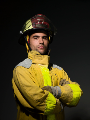 Portrait of a serious-looking Caucasian fireman standing in front of a fire engine parked at the station.