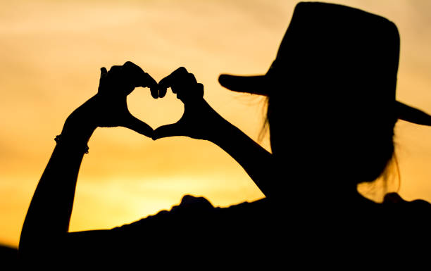 istock Girl making hearth shape, silhouette against golden sky 827758834