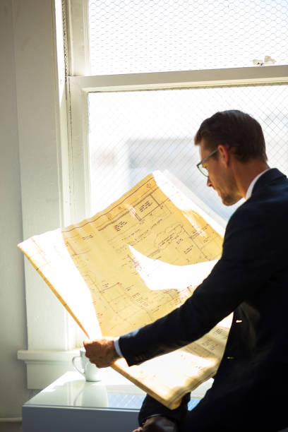 istock Man in Suit Looking at Old Blueprints in Window 827780934