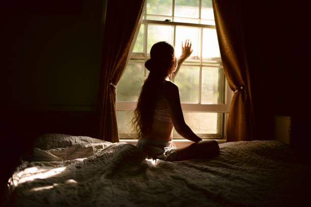 istock Young woman sitting on a bed by a window 827784068