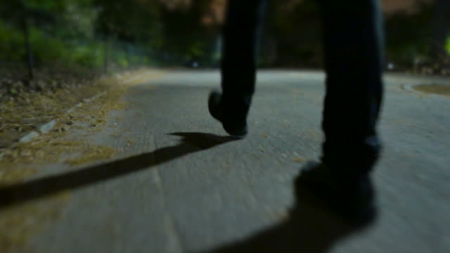 Young Man Walking in Spooky Scenery. Scary Atmosphere in a Park at Night. Close Up on Shoes. Shadows made by Street Lamps.