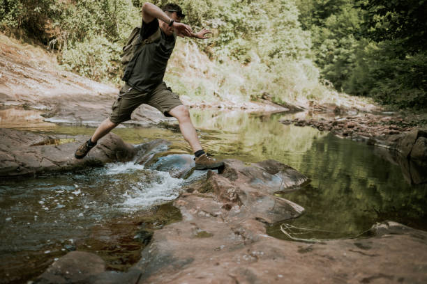 istock Young man hiking jumps over the mountain river 827788968