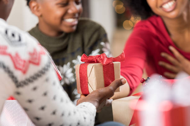 Man gives adult daughter a gift at Christmas Senior man gives his adult daughter a gift on Christmas Eve. She smiles while placing her hand over her heart. Her young son is sitting beside her. Focus is on the present. unwrapping stock pictures, royalty-free photos & images