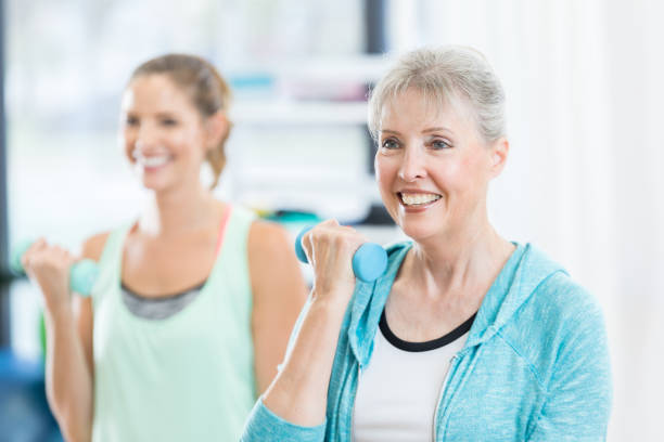 istock Senior woman works bicep with barbell during gym class 827810524