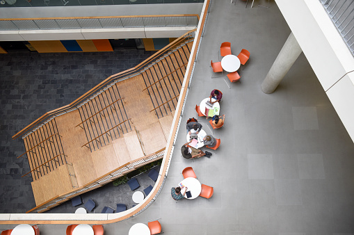 Group of students sitting at round tables, seen from above, with steps leading down from platform