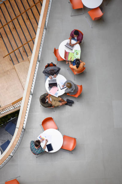 istock Students at modern college sitting at round tables using laptops and working 827810736