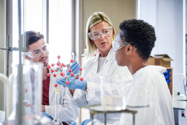 Two science students in laboratory wearing lab coats and safety goggles, learning about chemical structure