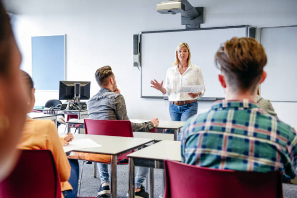 リスニ�ングのデスクで座っている学生と教室で大学講師 - england talking classroom education ストックフォトと画像