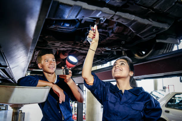 two student mechanics repairing car, woman using spanner - trainee working car mechanic imagens e fotografias de stock