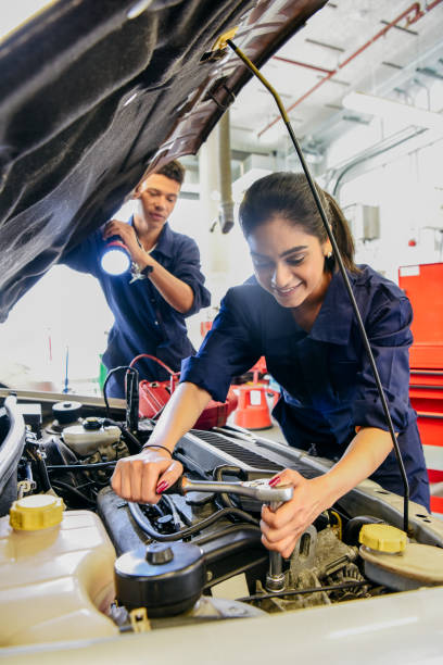 young female mechanic repairing car, man holding torch - trainee mechanic engineer student imagens e fotografias de stock