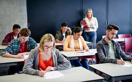 College lecturer standing at back of classroom as male and female students sit exam