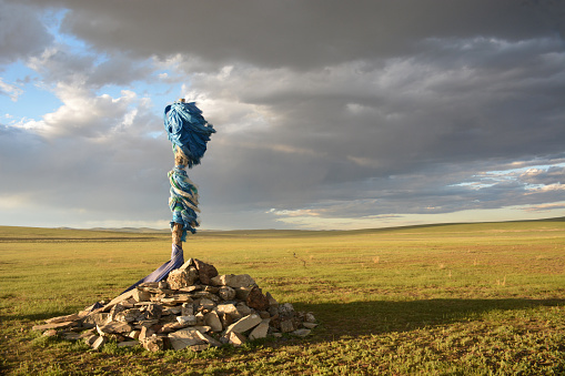 A shamanistic rock shrine stands in a field against a dramatic sky