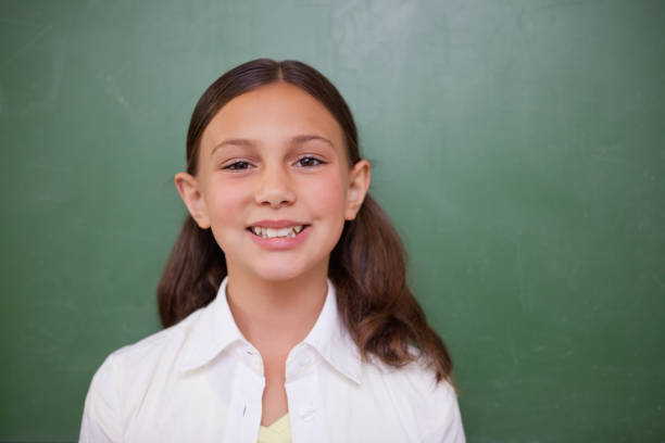Cute schoolgirl standing in front of a blackboard in a classroom