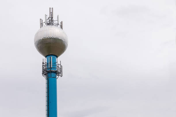 Water management or irrigation facility featuring a canal, control structure, and a small utility building, with a communication tower in the background. Outdoor infrastructure scene captured in clear daylight, suitable for concepts of water resources, public utilities, infrastructure, technology, sustainability, and environmental management.