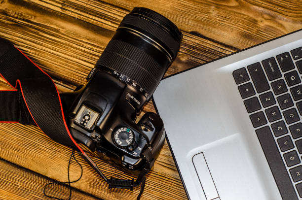 istock Modern DSLR camera and laptop on wooden table. Top view 827848308