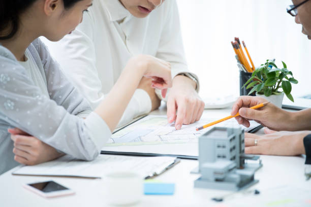 The customer and the employee are discussing the materials by looking at the materials. A couple and employees are talking while looking at the materials in the meeting table where the model of the house is placed. real estate office photos stock pictures, royalty-free photos & images