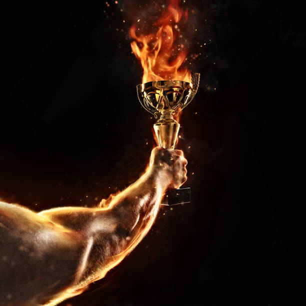 istock Muscular man arm holding burning trophy cup on black background 827881568