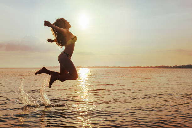 Young Woman Jumps on lake Beach at sunset