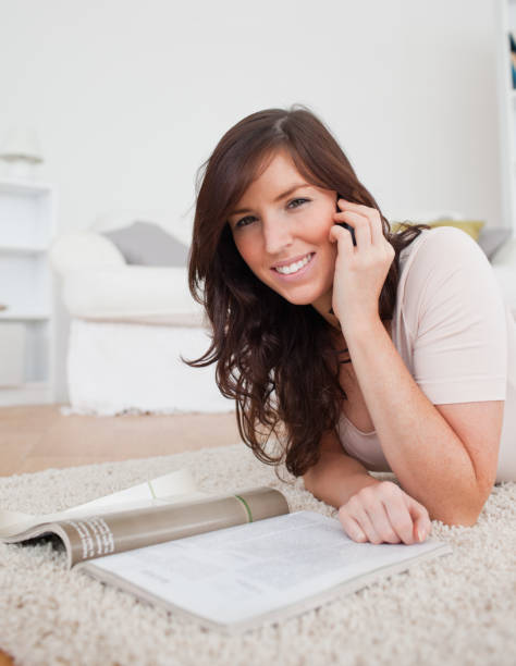 istock Young charming female reading a magazine while lying on a carpet 827887278