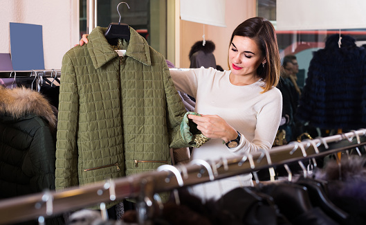 Young european woman choosing green quilted jacket in women`s cloths store
