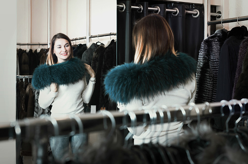 Pretty woman customer examining new fur neckpiece in women`s cloths store