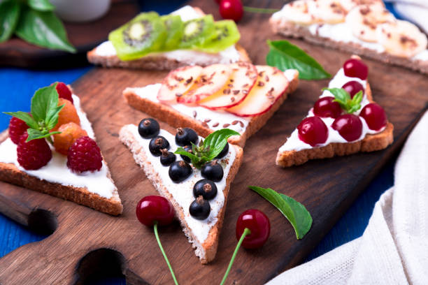 istock Fruit toast on wooden board on blue rustic background. Healthy breakfast. Clean eating. Dieting concept. Grain bread slices with cream cheese and various fruit, berries, seeds. Vegetarian. 827895782