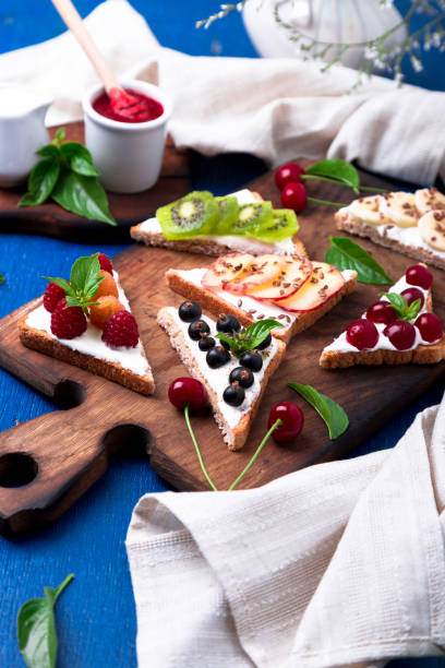 istock Fruit toast on wooden board on blue rustic background. Healthy breakfast. Clean eating. Dieting concept. Grain bread slices with cream cheese and various fruit, berries, seeds. Vegetarian. 827895856