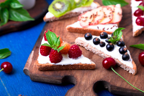 istock Fruit toast on wooden board on blue rustic background. Healthy breakfast. Clean eating. Dieting concept. Grain bread slices with cream cheese and various fruit, berries, seeds. Vegetarian. 827895874