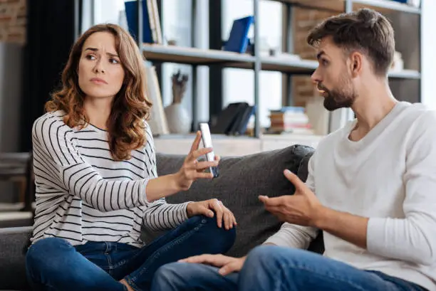 Photo of Unhappy young woman showing a phone to her boyfriend