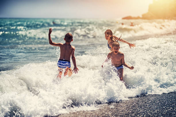 niños disfrutando de enormes olas en la playa - spraying beaches summer sunlight fotografías e imágenes de stock