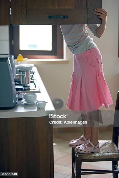 Girl Standing On Chair Looking In Kitchen Cupboard Stock Photo - Download Image Now - Cabinet, On Top Of, Searching