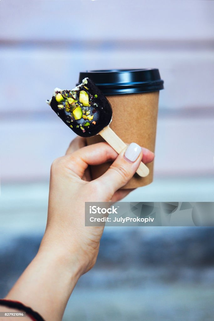 Woman's hand holding chocolate popsicle Woman's hand holding chocolate popsicle ice cream and coffee cup Adult Stock Photo