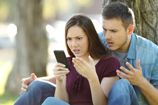 Photo of Angry couple using a smart phone outdoors