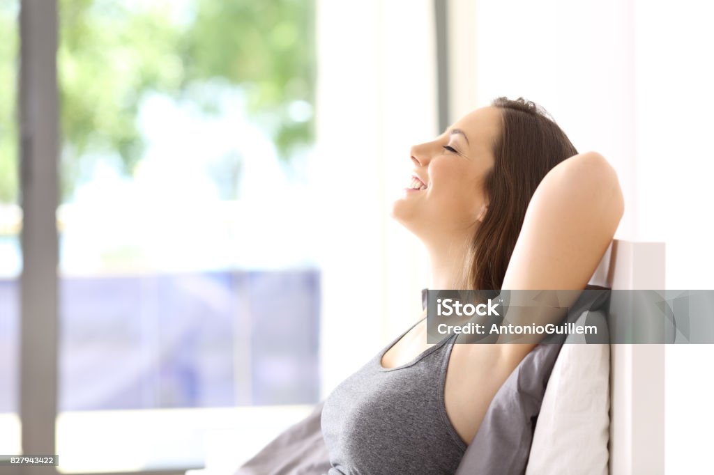 Woman relaxing on the bed in an hotel room Side view portrait of a single happy woman relaxing sitting on the bed of an hotel room or home Non-Urban Scene Stock Photo