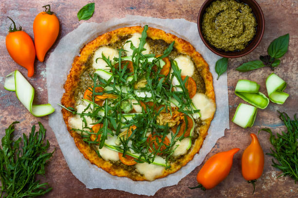 istock Cauliflower pizza crust with pesto, yellow tomatoes, zucchini, mozzarella cheese and squash blossom. 827951794