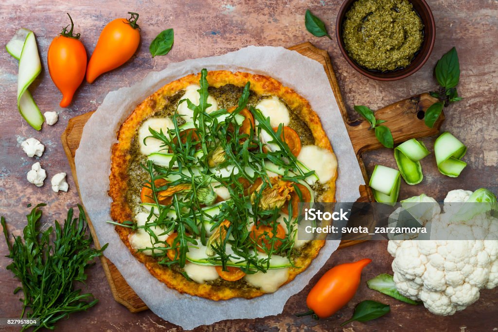 Cauliflower pizza crust with pesto, yellow tomatoes, zucchini, mozzarella cheese and squash blossom. Pizza Stock Photo