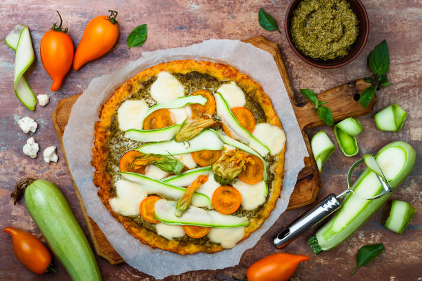 istock Cauliflower pizza crust with pesto, yellow tomatoes, zucchini, mozzarella cheese and squash blossom. 827951836