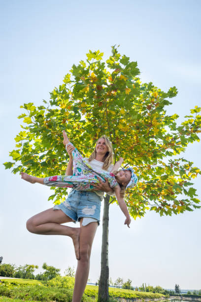 mutter beschäftigt sich mit yoga mit ihrer kleinen tochter lachen - yoga good posture women little girls stock-fotos und bilder