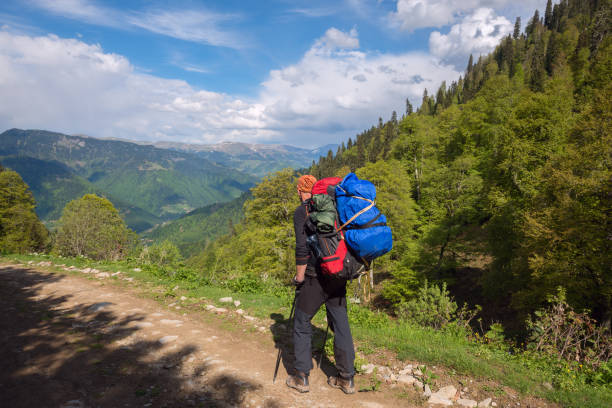istock Man adventurer with big backpack goes along the mountain road 827984144