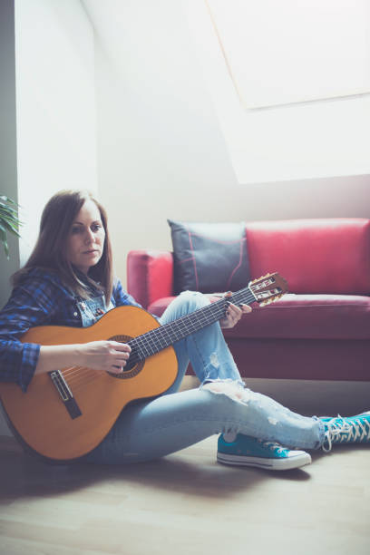 istock Young hipster girl playing guitar at cozy home interior 827991330