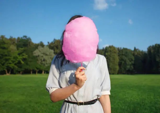 young pretty brunette woman hold pink cotton candy near her face outdoor on nature