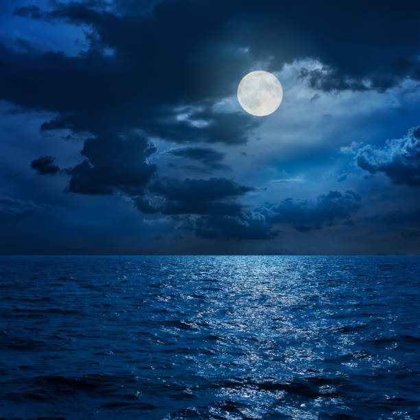 Photo of full moon in clouds over sea in night