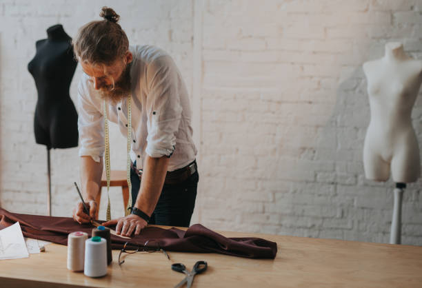 Handsome blonde bearded man leaning upon worktable with equipment holding pencil and ruler.
