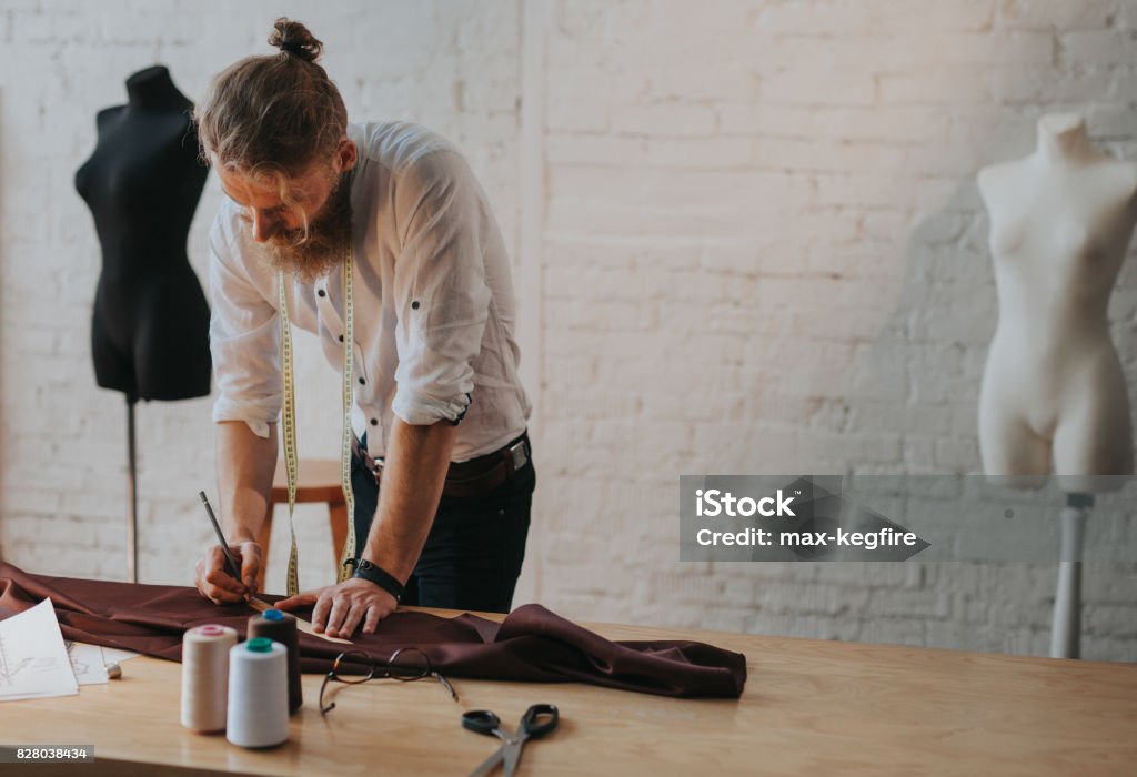 Bearded man leaning upon worktable Handsome blonde bearded man leaning upon worktable with equipment holding pencil and ruler. Fashion Stock Photo