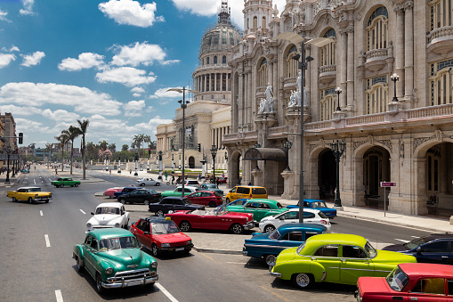 Vintage American cars driving through the streets in Havana Vieja, Cuba. Gran Teatro de La Habana in traditional colonial style are visible in the background, 50 megapixel image.