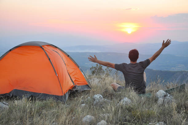 istock Man raised his hands and enjoy the sunset next to a tent. 828073588