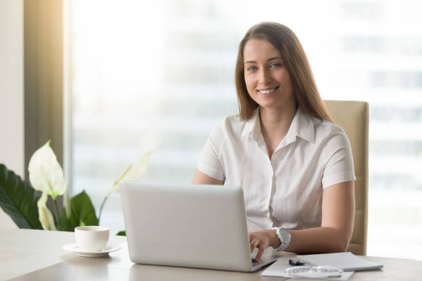 istock Pretty businesswoman working on laptop, smiling for camera at workplace 828110406