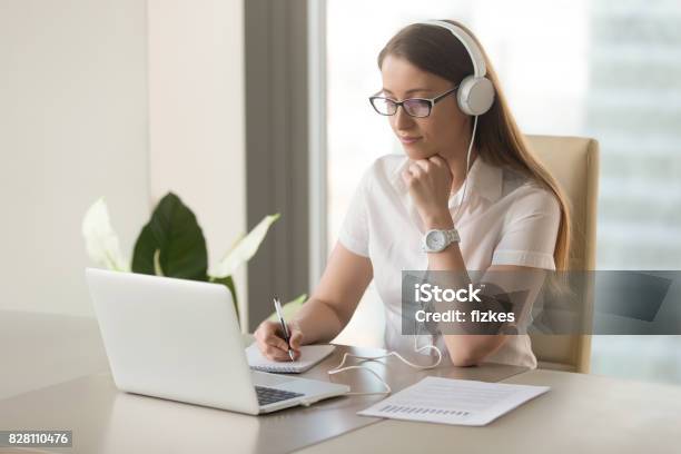 Focused Attentive Woman Wearing Headphones Using Laptop At Office Desk Stock Photo - Download Image Now
