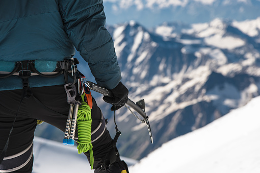 Close up A young guy climber holds in his hand an ice ax standing on the summit high in the mountains against the background of snow-covered Caucasian rocks. Extreme sport concept